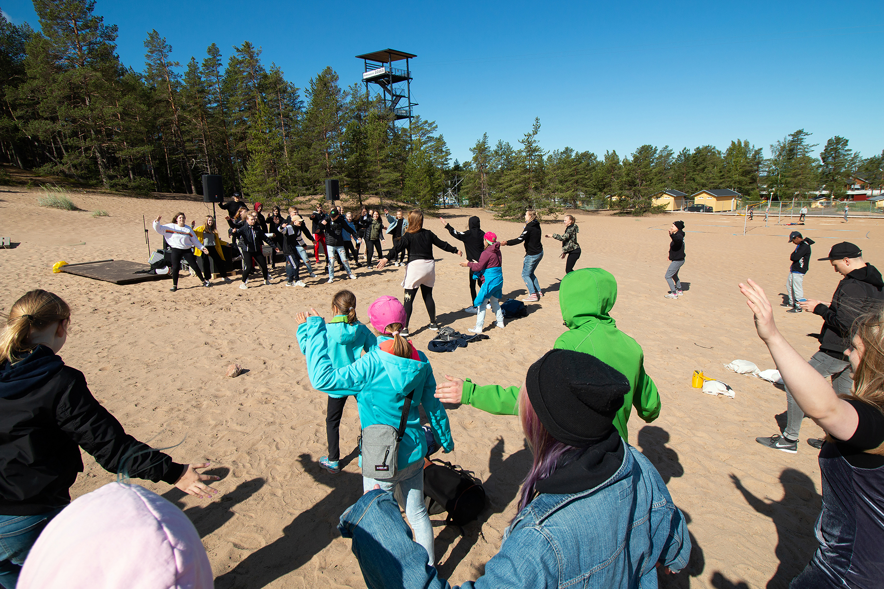 Joukko nuoria harrastaa liikuntaa hiekkarannalla.