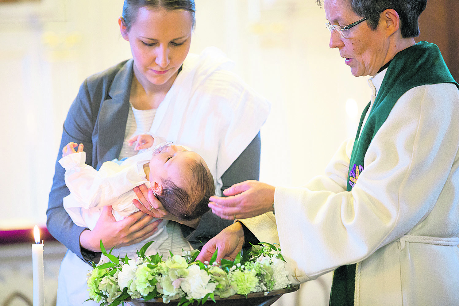 Pappi toimittaa kastetta, vauva kummin sylissä.